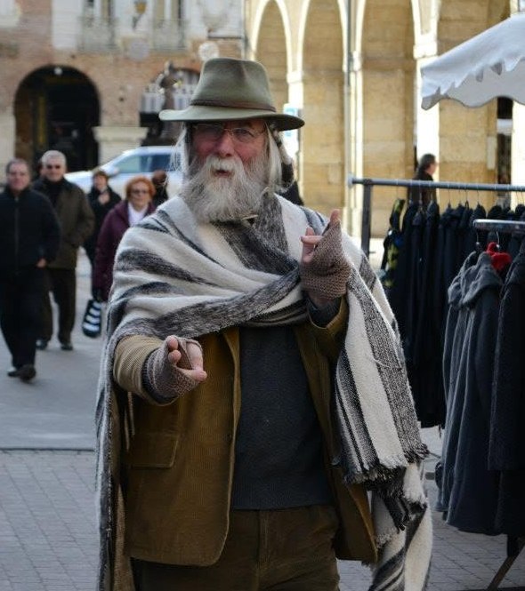 Chris Whittington, in a hat and woven shawl in a market square